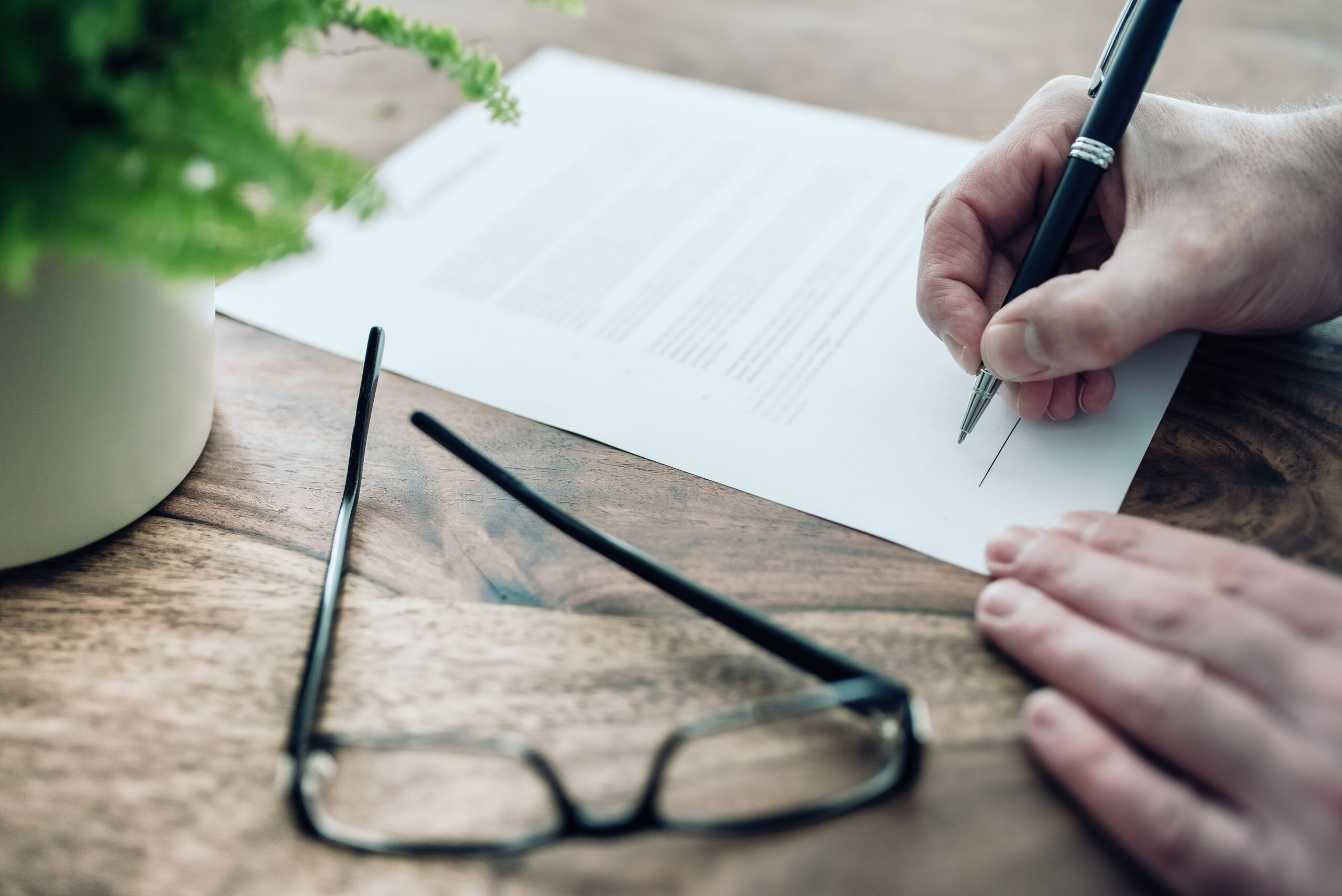 Vue rapprochée d'une personne en train de signer une clause bénéficiaire avec un stylo sur un bureau en bois