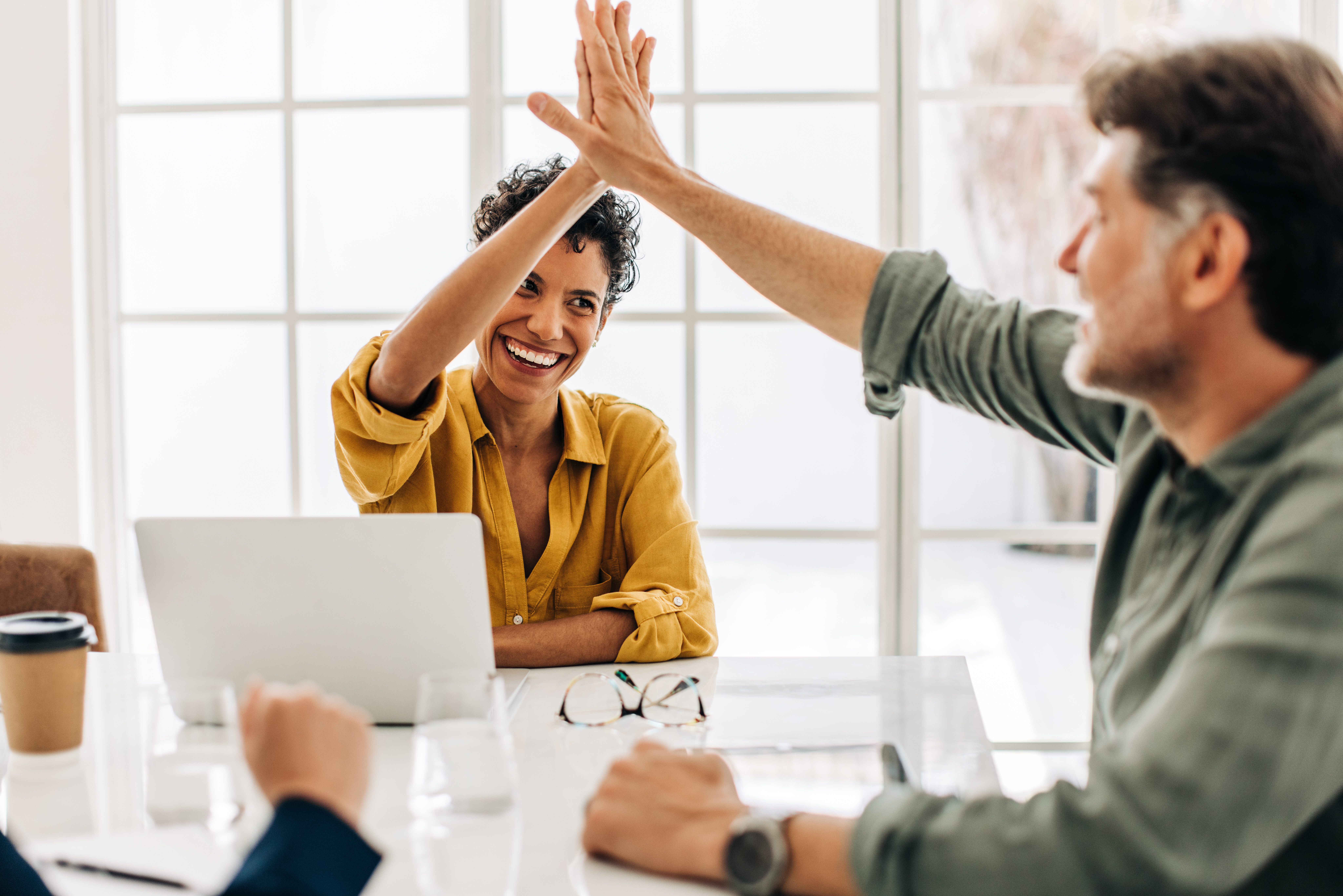 Deux personnes se tapant dans la main, assis autour d'un bureau. Illustrant la réussite de la collaboration lors de la gestion déléguée